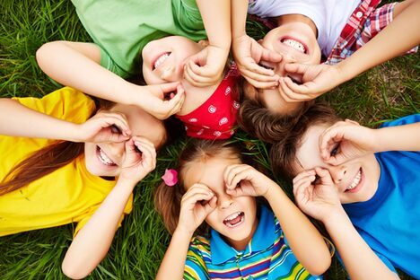 Lachende Kinder liegen Kopf an Kopf auf einer Wiese.